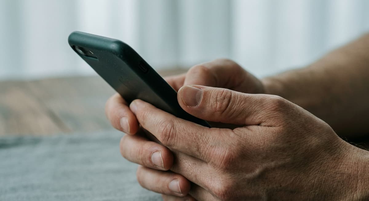 a close crop of hands holding a smartphone with the screen out of frame, neutral background