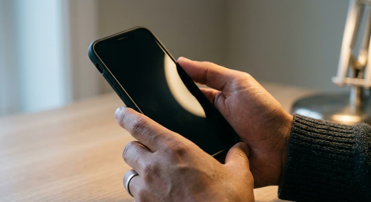 a close crop of hands holding a smartphone with the screen out of frame, neutral background