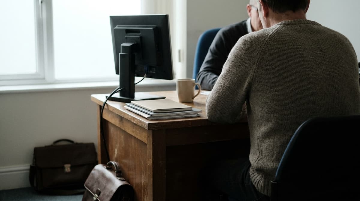 a person sitting with a GP in a plain consulting room, seen from behind the patient, no readable text or charts
