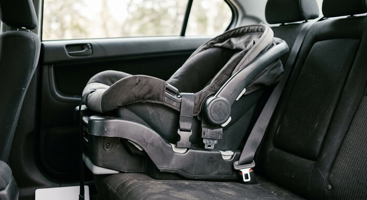 an empty infant car seat carrier clicked into its base on a back seat