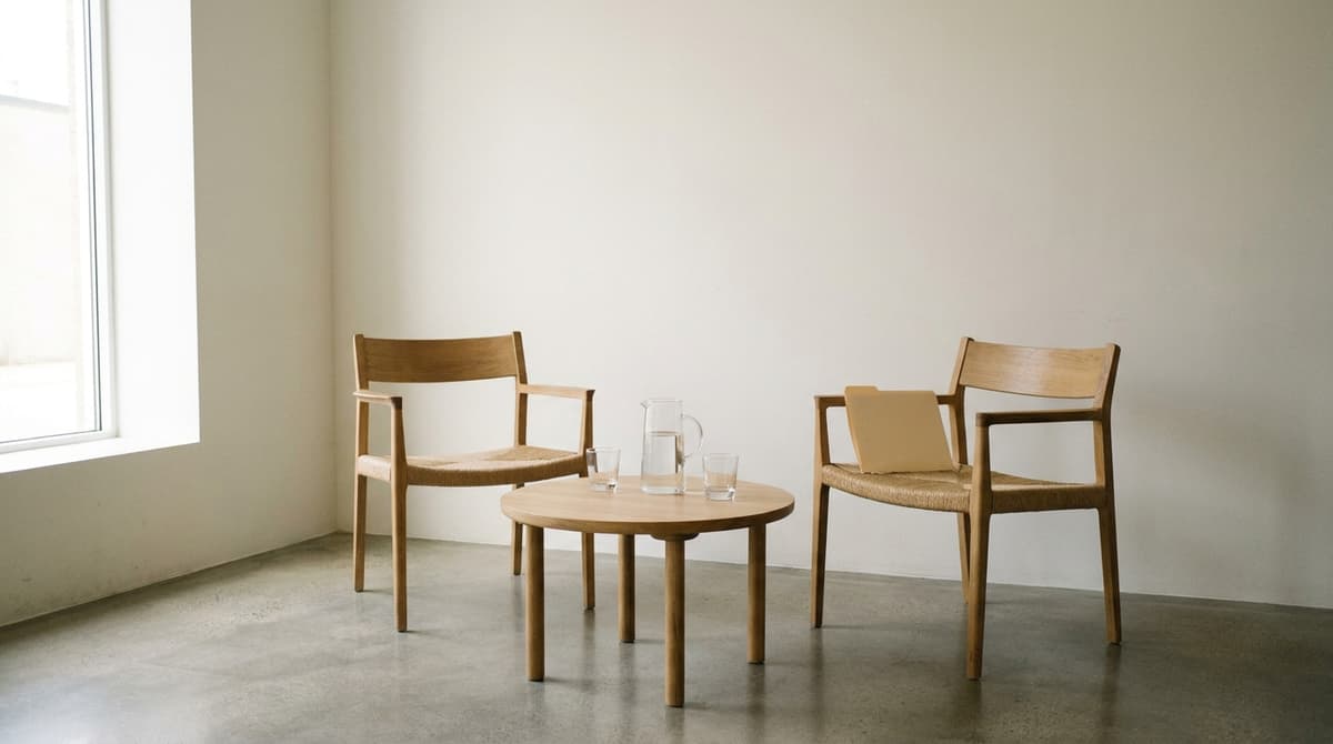 Two wooden armchairs facing across a small round table with a water jug, glasses and a closed folder