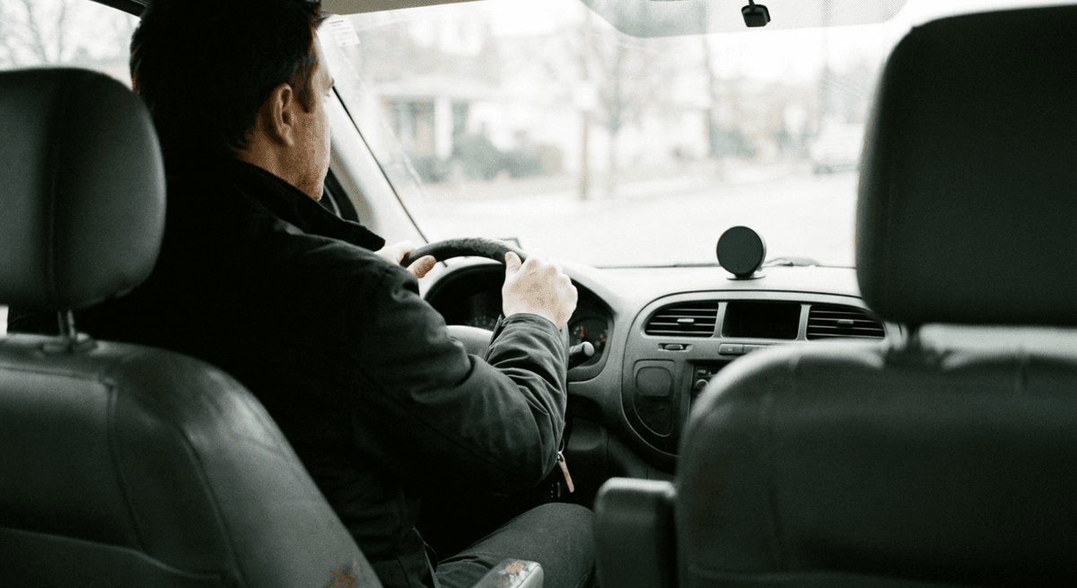 delivery driver at the wheel of a work van with a small black tracking puck on the dashboard