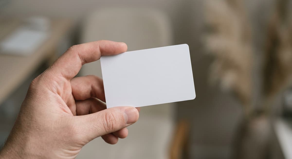 a close crop of a hand holding a blank plastic card, background bokeh, neutral tones
