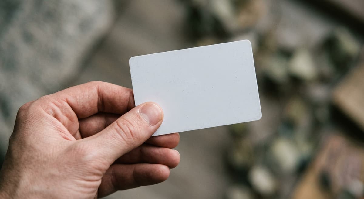 a close crop of a hand holding a blank plastic card, background bokeh, neutral tones