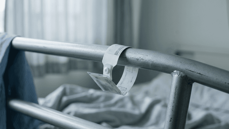 Delaware patient wristband on a hospital bed railing, close-up