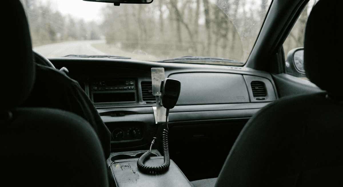Handheld coiled-cord microphone on a metal clip on a patrol-style dashboard, seen from the back seat