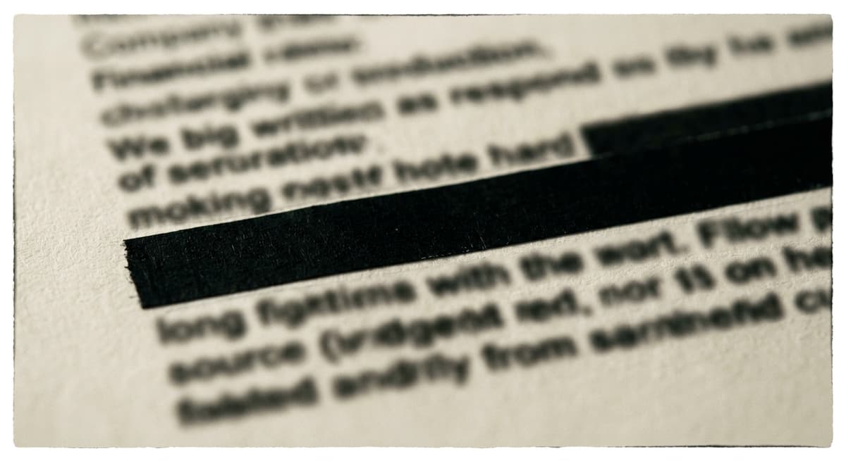 a black rectangle of redaction tape over lines of blurred text on a printed page, extreme close-up