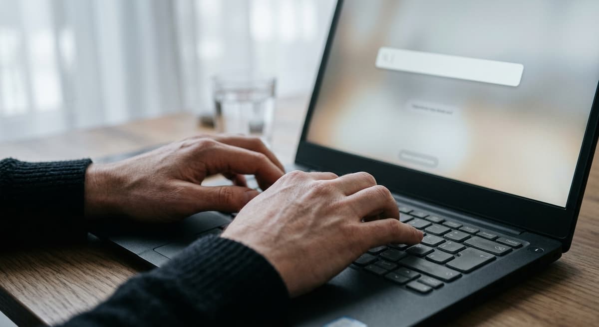 a close crop of hands typing on a laptop keyboard with a simple blank search bar visible on the screen, shallow depth of