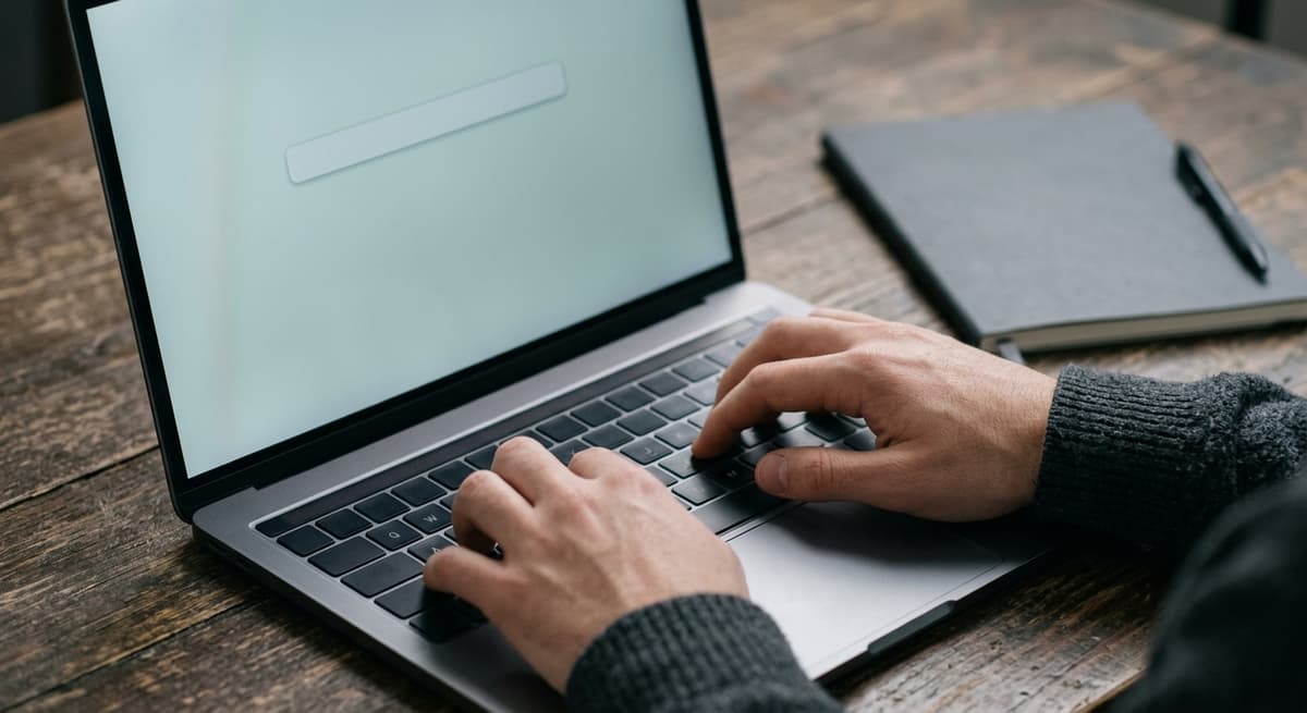 a close crop of hands typing on a laptop keyboard with a simple blank search bar visible on the screen, shallow depth of