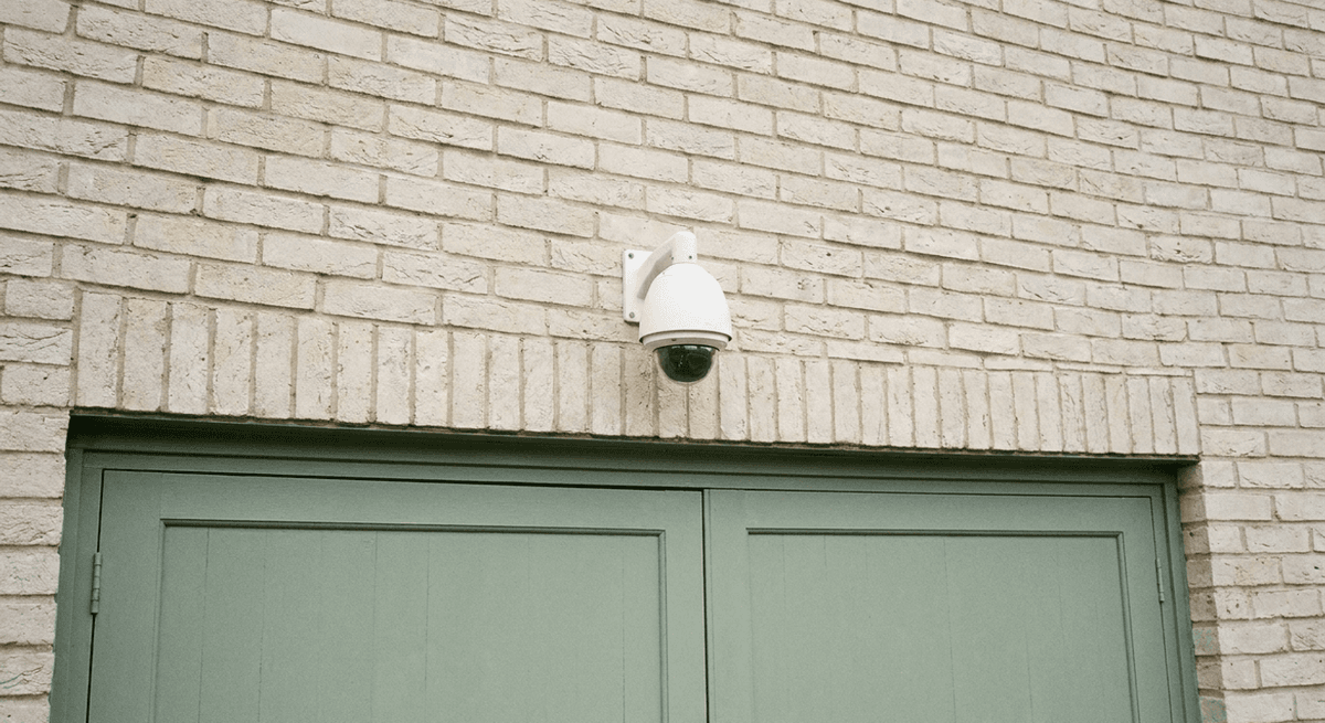 Cámara de seguridad domo blanca montada en una pared de ladrillo sobre una puerta de garaje verde