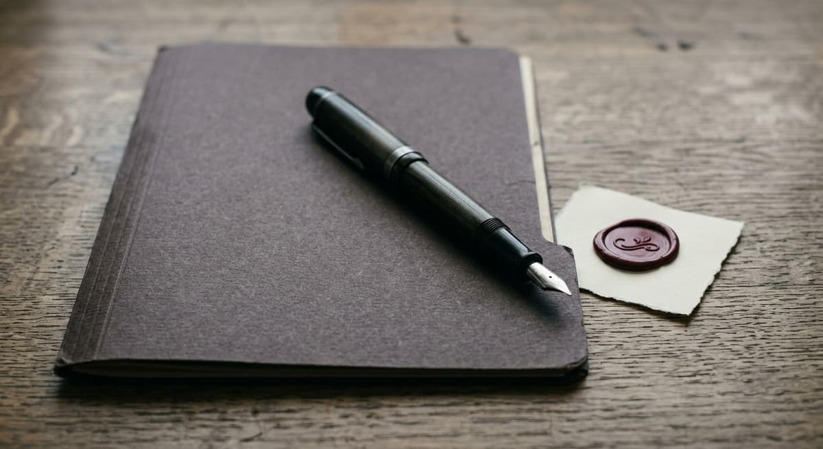 fountain pen resting on a closed folder beside a wax seal