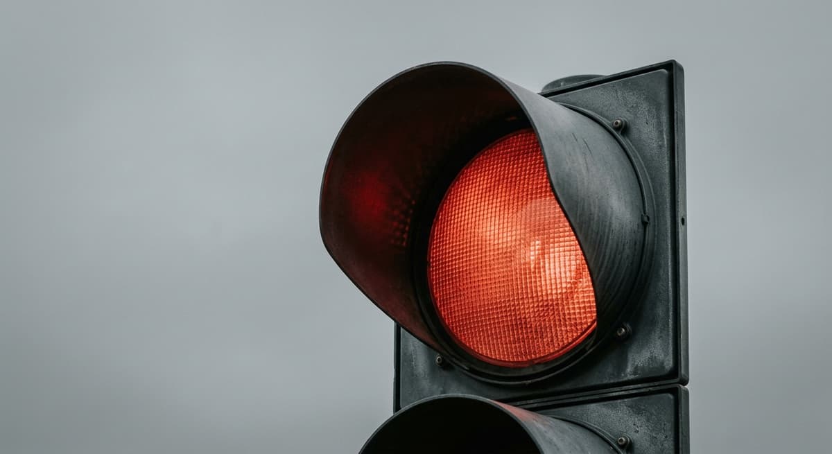 a close crop of a traffic signal head showing the red lens illuminated against an overcast sky