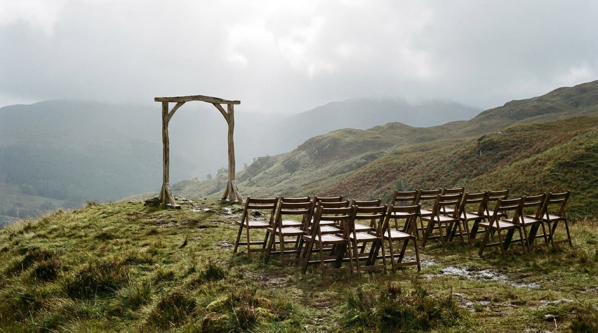 an outdoor wedding setting on a Scottish hillside with a simple wooden arch and rows of empty chairs, misty hills behind, no people