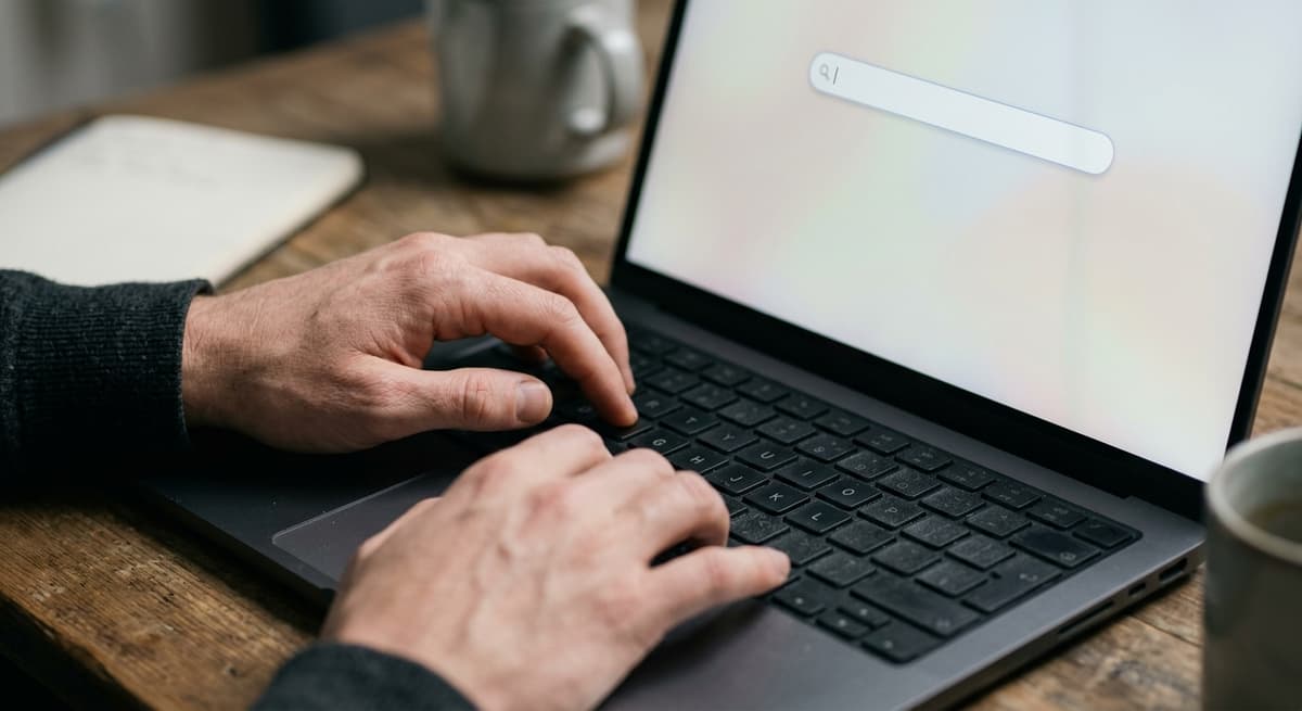 a close crop of hands typing on a laptop keyboard with a simple search bar visible on the screen, shallow depth of field