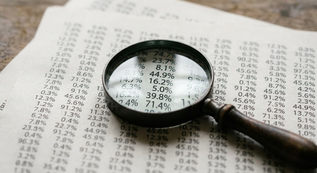 a magnifying glass lying on a dense printed table of percentage figures, digits softly blurred
