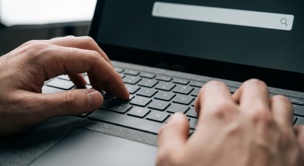 a close crop of hands typing on a laptop keyboard with a simple search bar visible on the screen, shallow depth of field