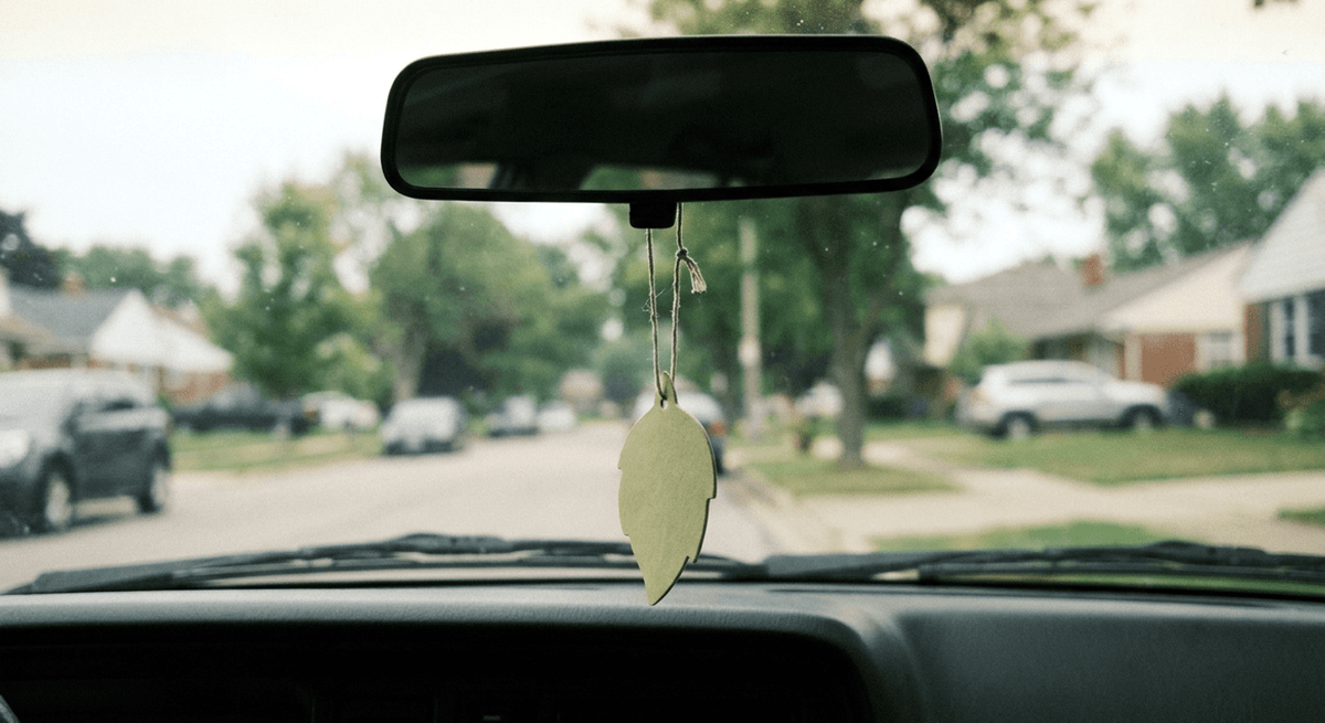 A plain leaf-shaped air freshener hanging from a car rearview mirror, viewed through the windshield